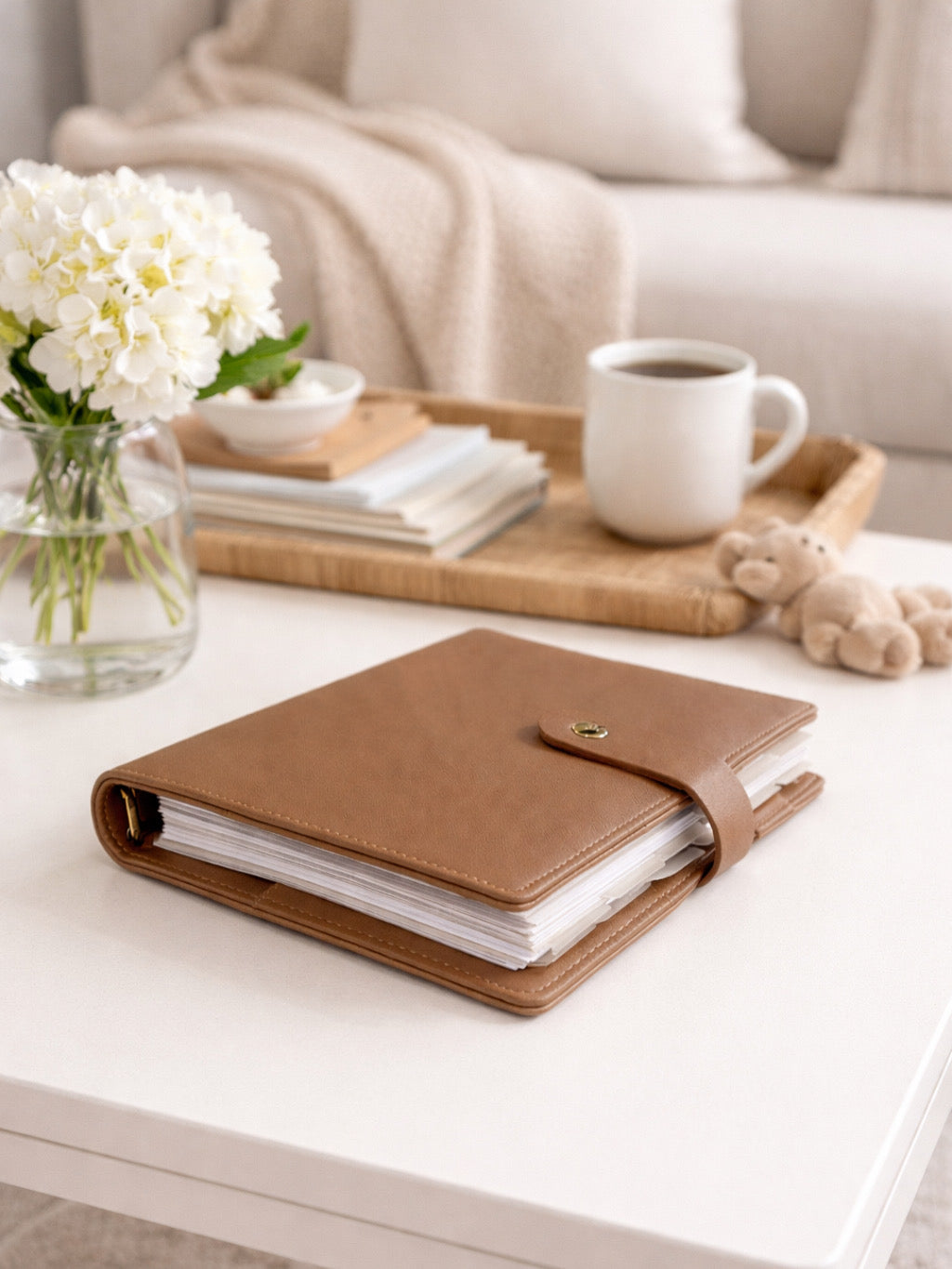 Brown leather parent organiser on a white surface with a cup of coffee, flowers, and books in the background.