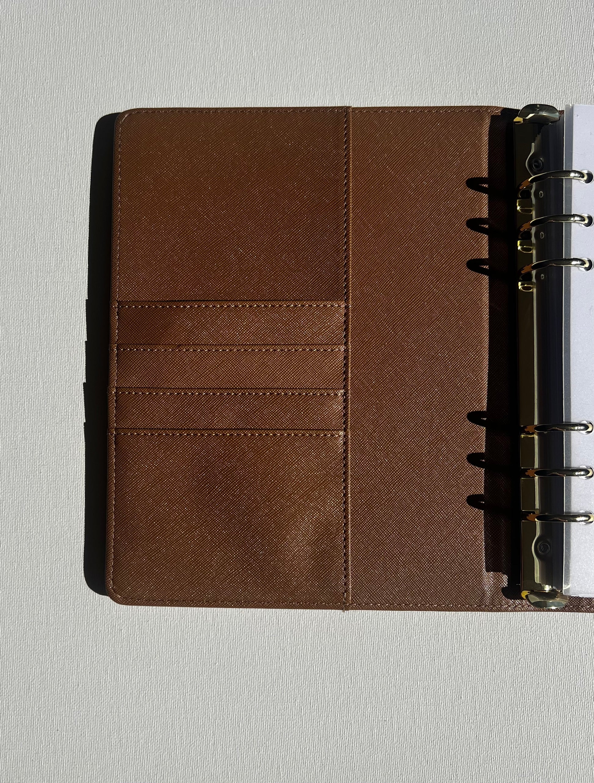 Brown leather notebook with gold ring binding on a light gray background