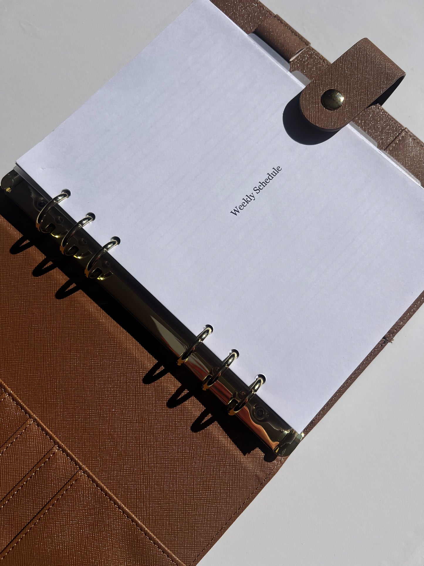 Brown planner with a white page labeled 'Weekly Schedule' on a light gray background