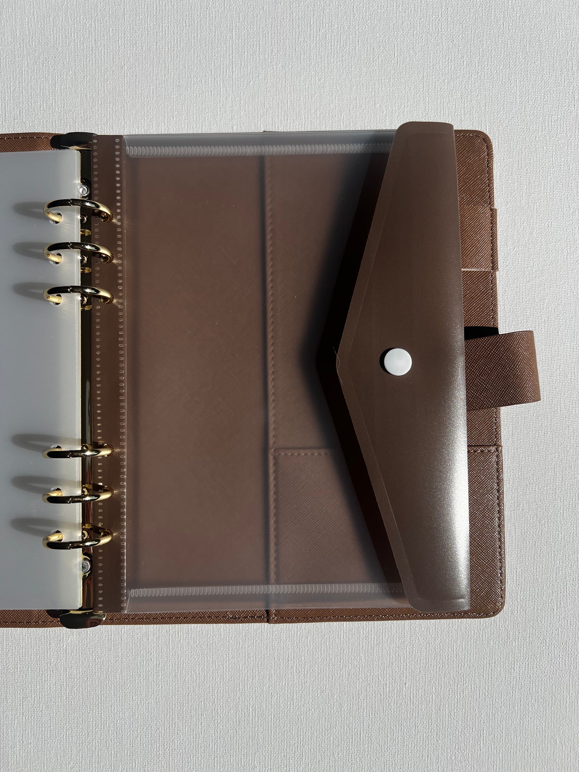 Brown tan leather planner with clear plastic folder clipped into binder with brown clip flap
