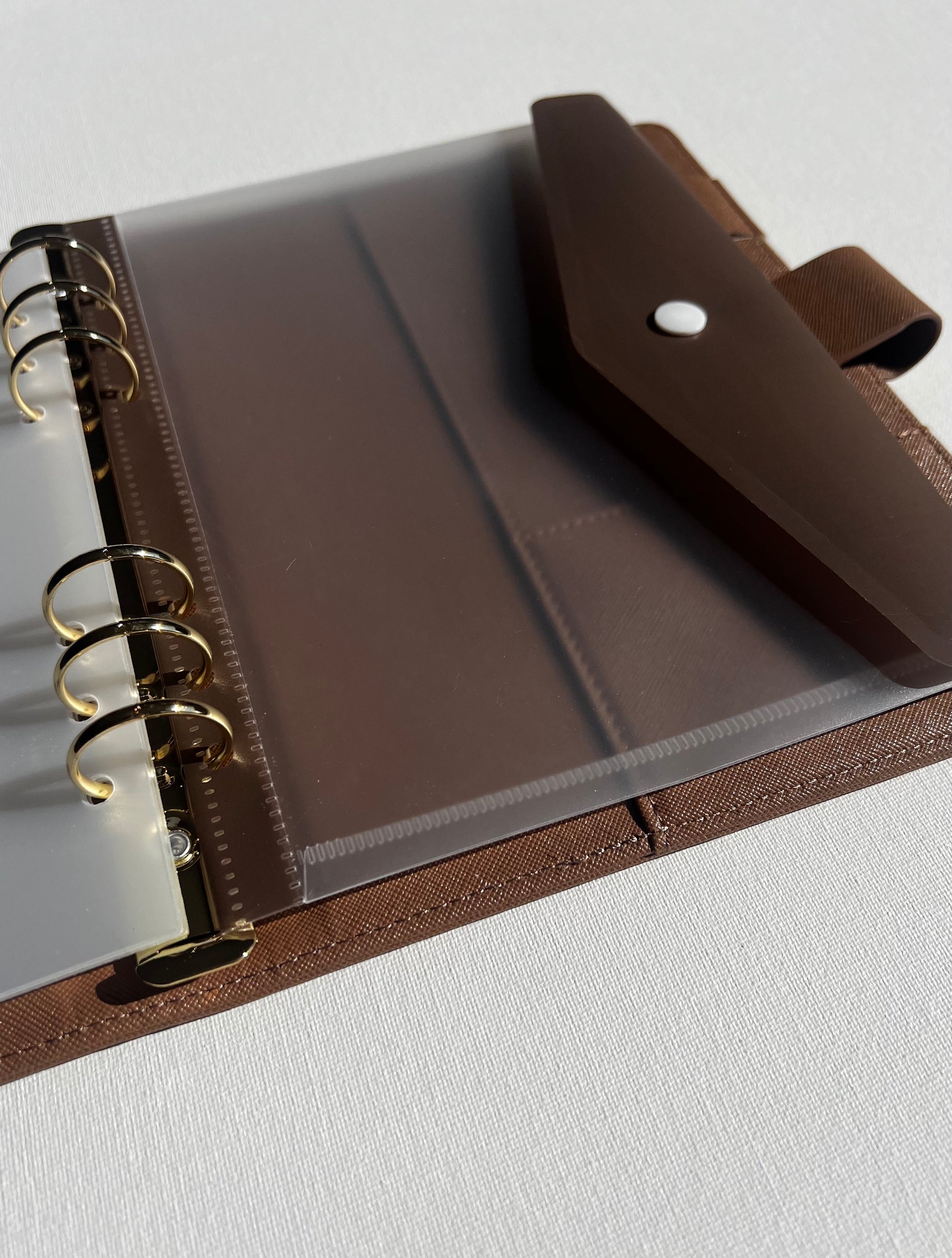 Brown tan leather planner with clear plastic folder clipped into binder with brown clip flap