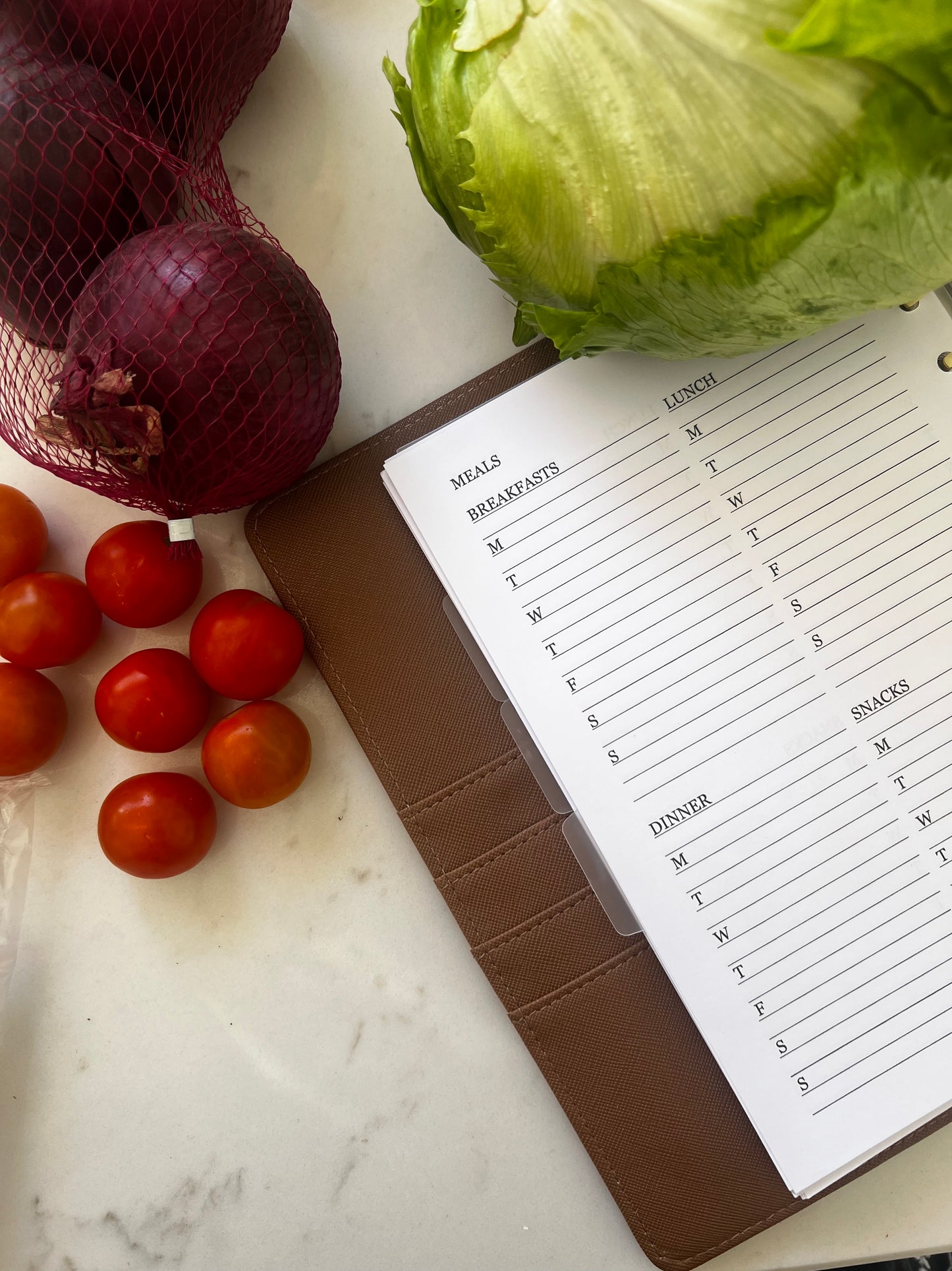Notebook with meal planning list next to vegetables on a marble surface