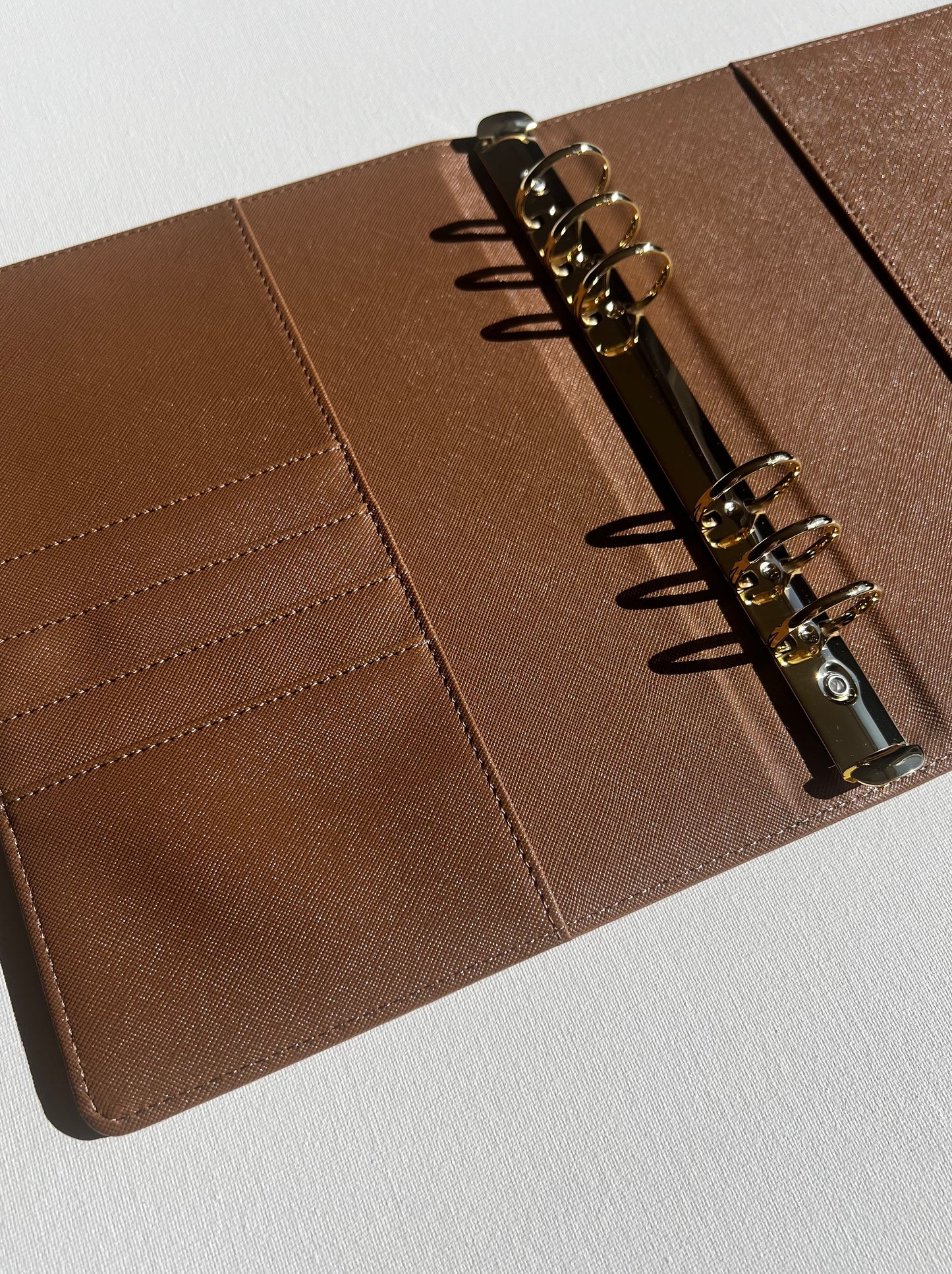 Brown leather notebook with gold metal rings on a white background